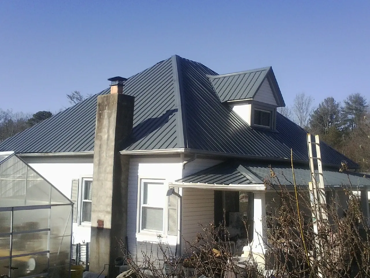 Dark blue standing seam metal roof on a white farmhouse with dormer — Slate & Tile Roof Repair by Roofing Brothers in Moulton