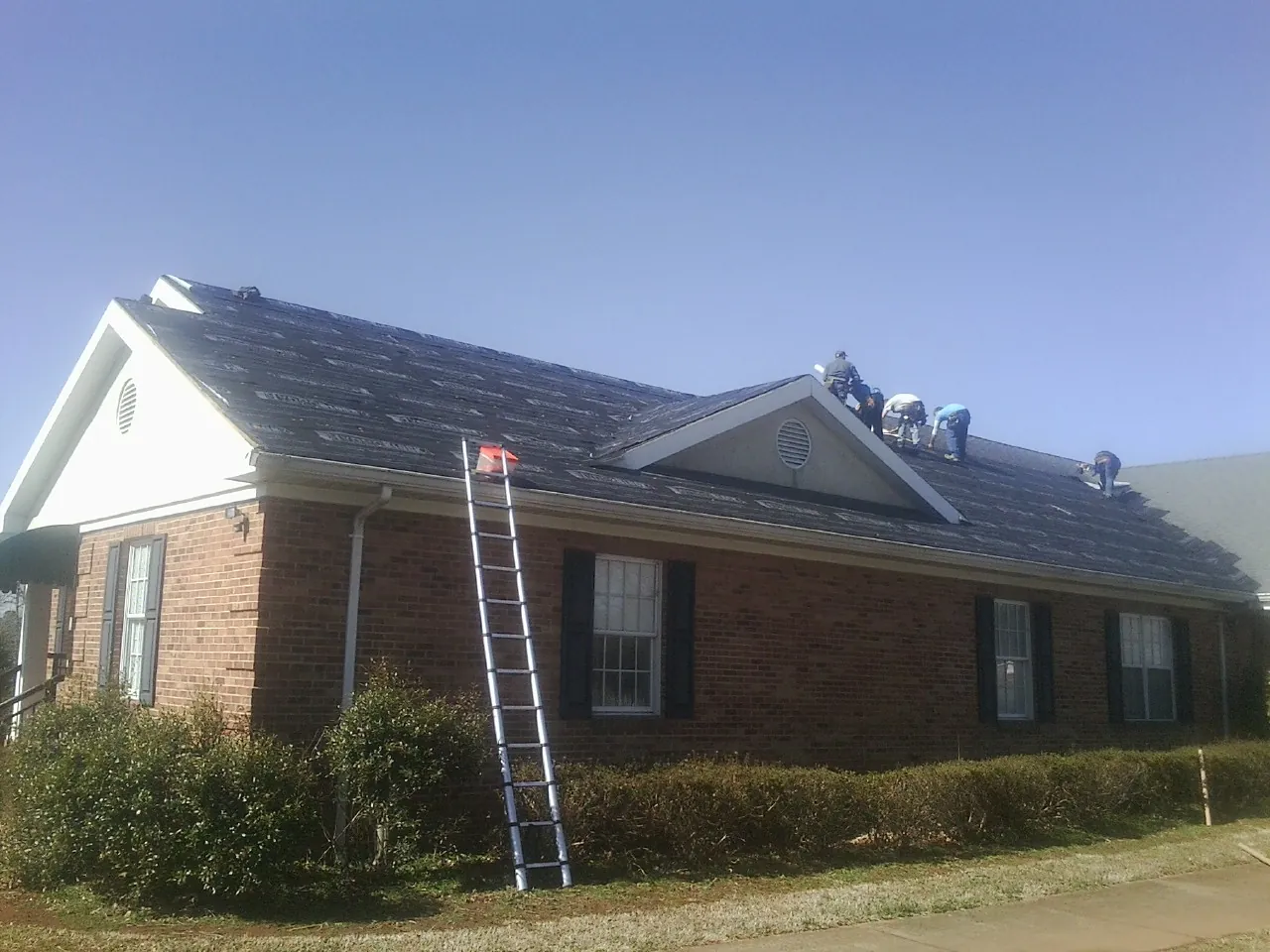Crew tearing shingles off a brick ranch roof with a ladder set — Metal Roof Repair work by our crew in Moulton