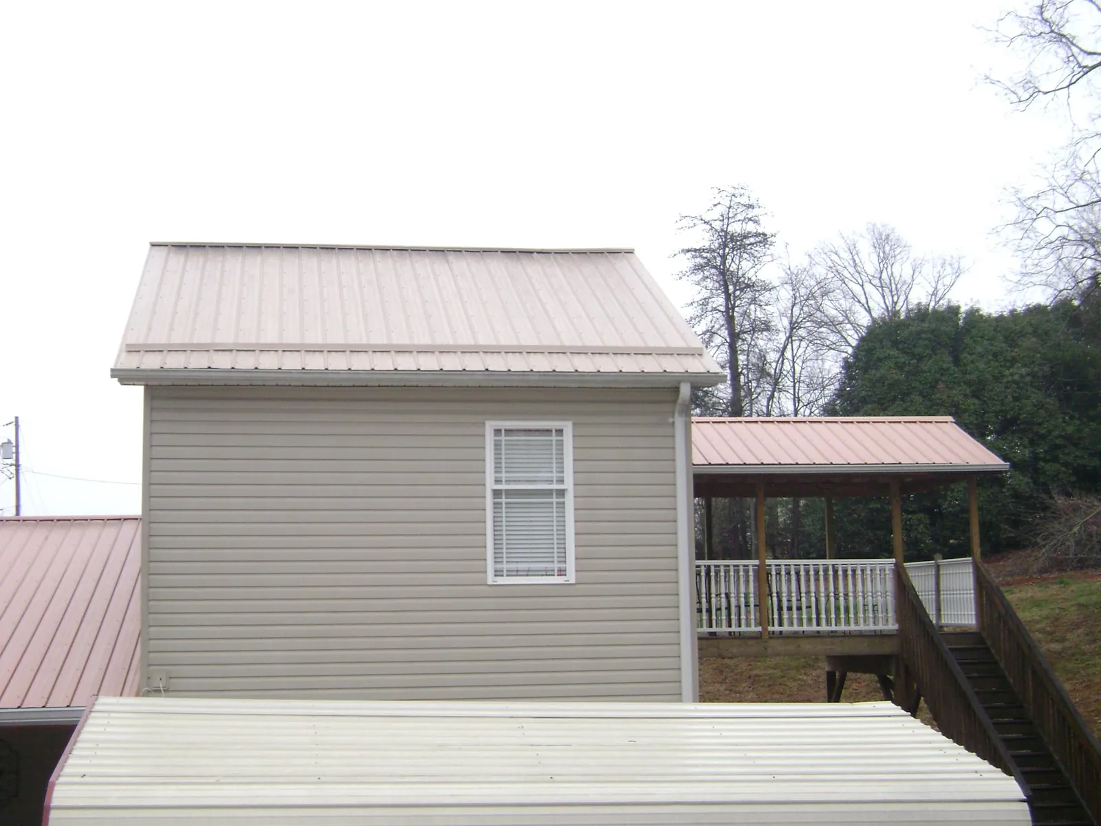 Tan metal roofs on a two story addition and attached porch, from a Roof Replacement job in Moulton